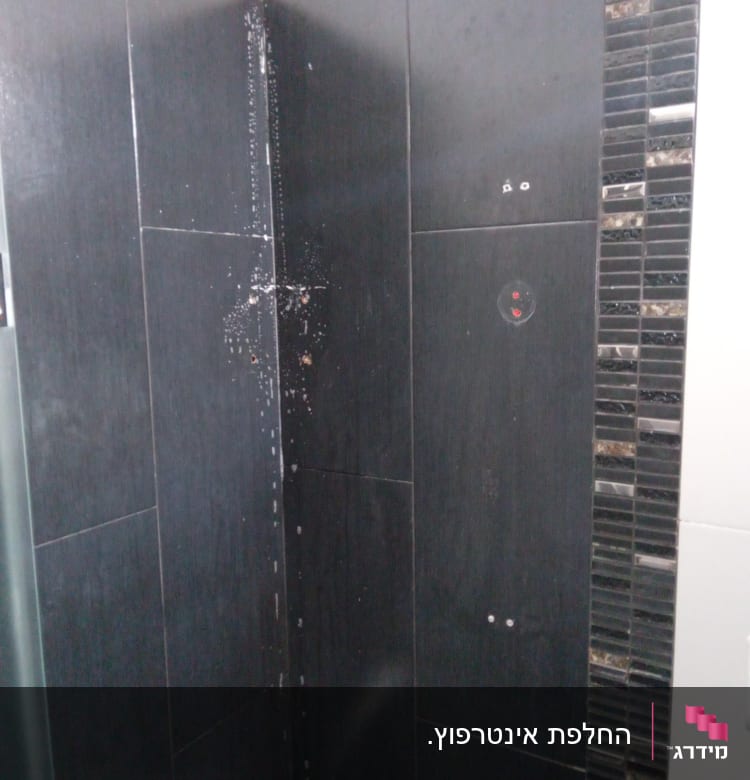קיר מקלחת עם אריחים שחורים וברז מתכת